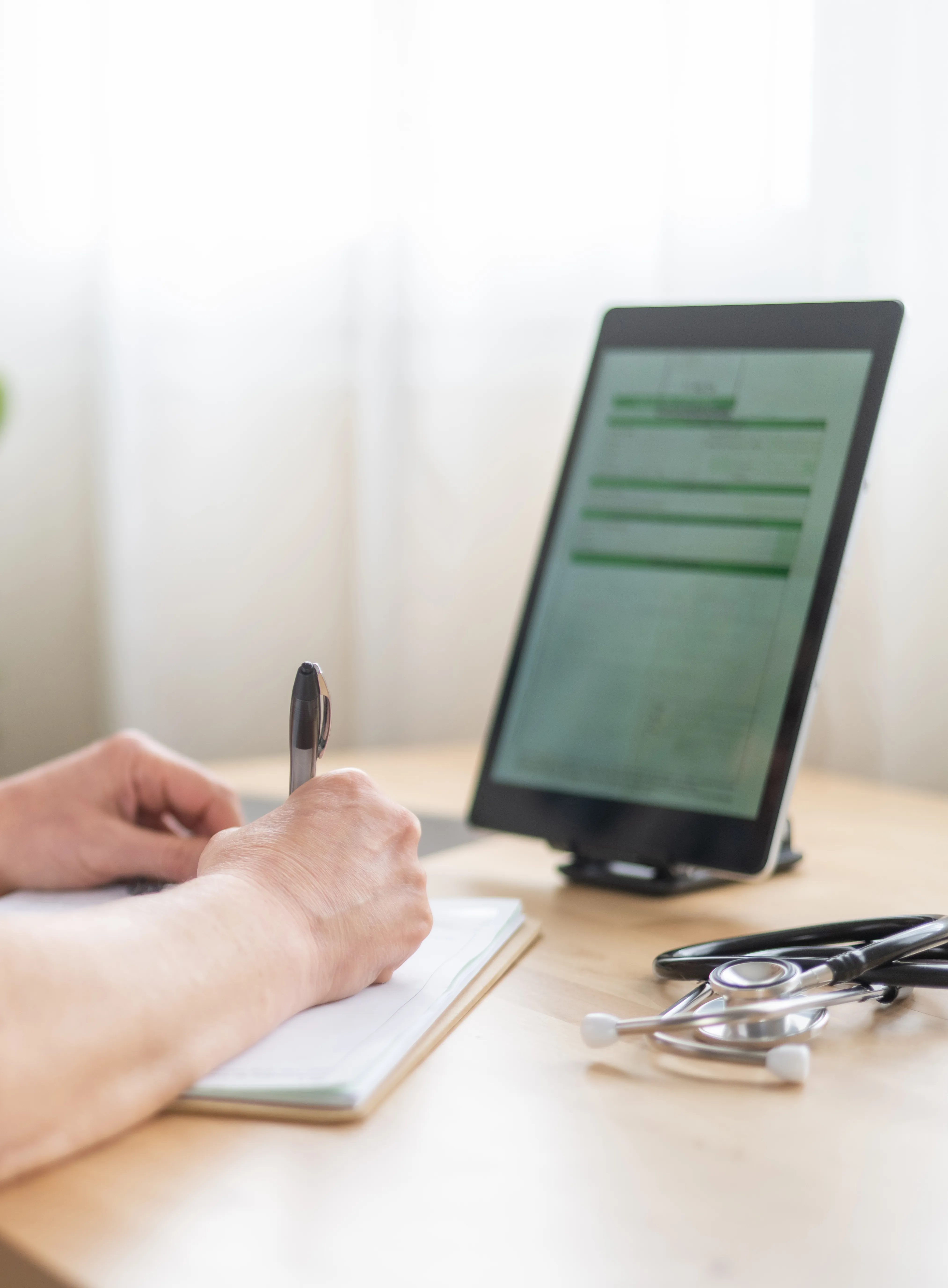 Licensed physician reviewing a patient chart on a tablet while taking notes
